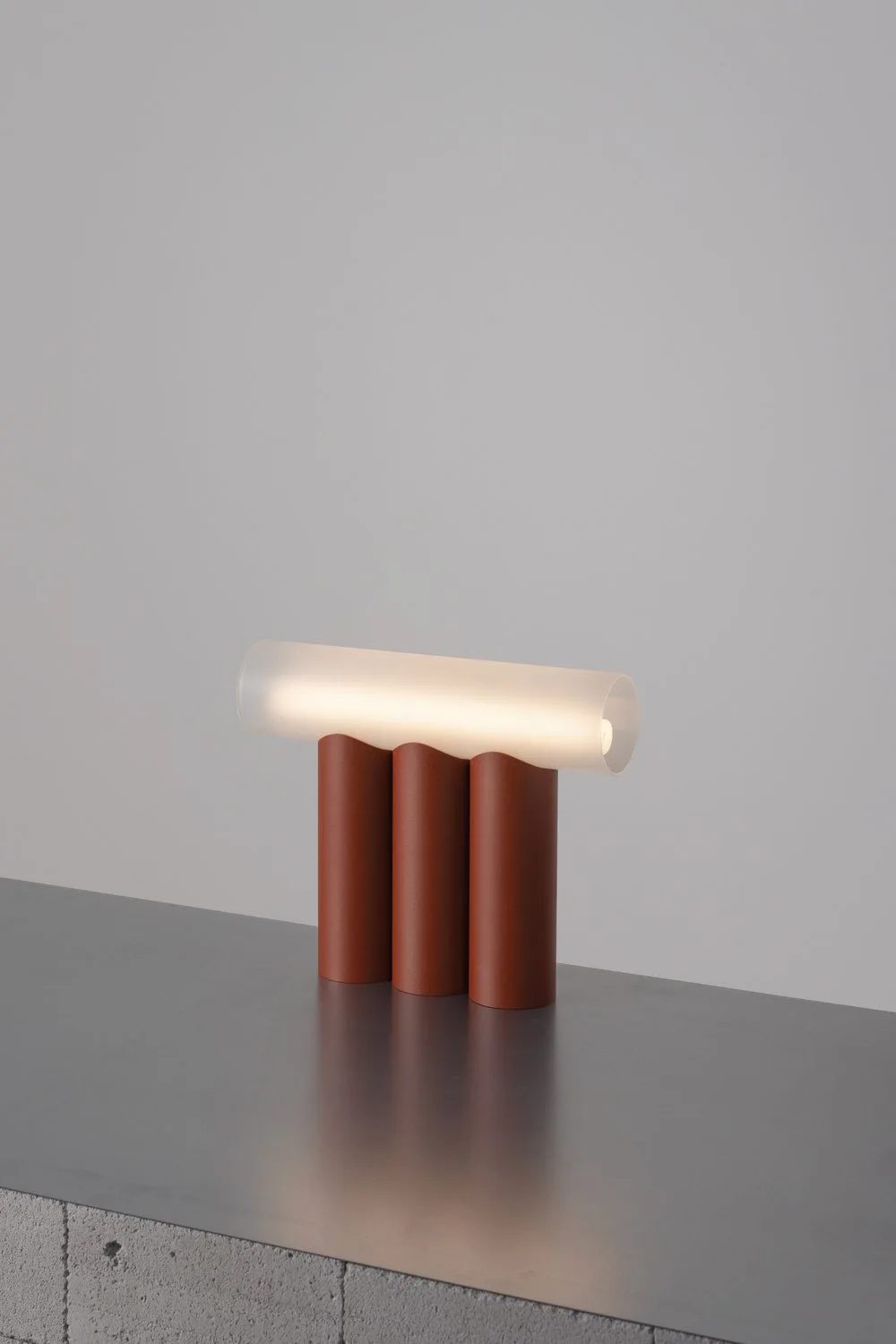 Luminaire de la série Multitude, du studio paulineplusluis : un tube lumineux posé sur des colonnes terracotta.
